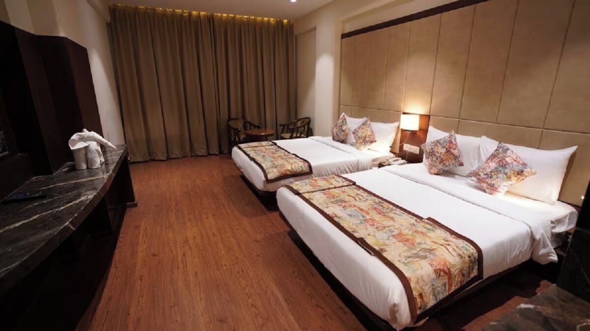 Ein Hotelzimmer mit zwei Betten, Holzboden, Fernseher, Schreibtisch und einem Fenster mit Vorhängen.