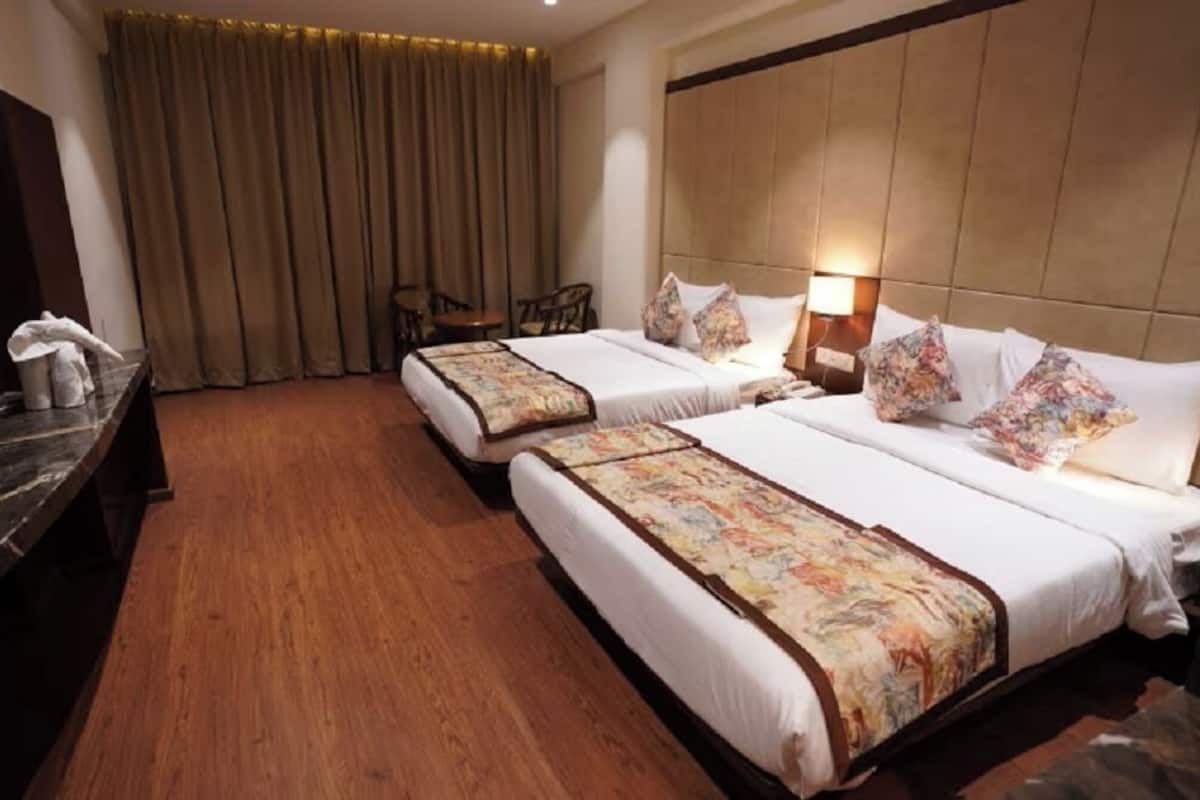 Habitación de hotel con dos camas, piso de madera, televisor, escritorio y ventana con cortinas.