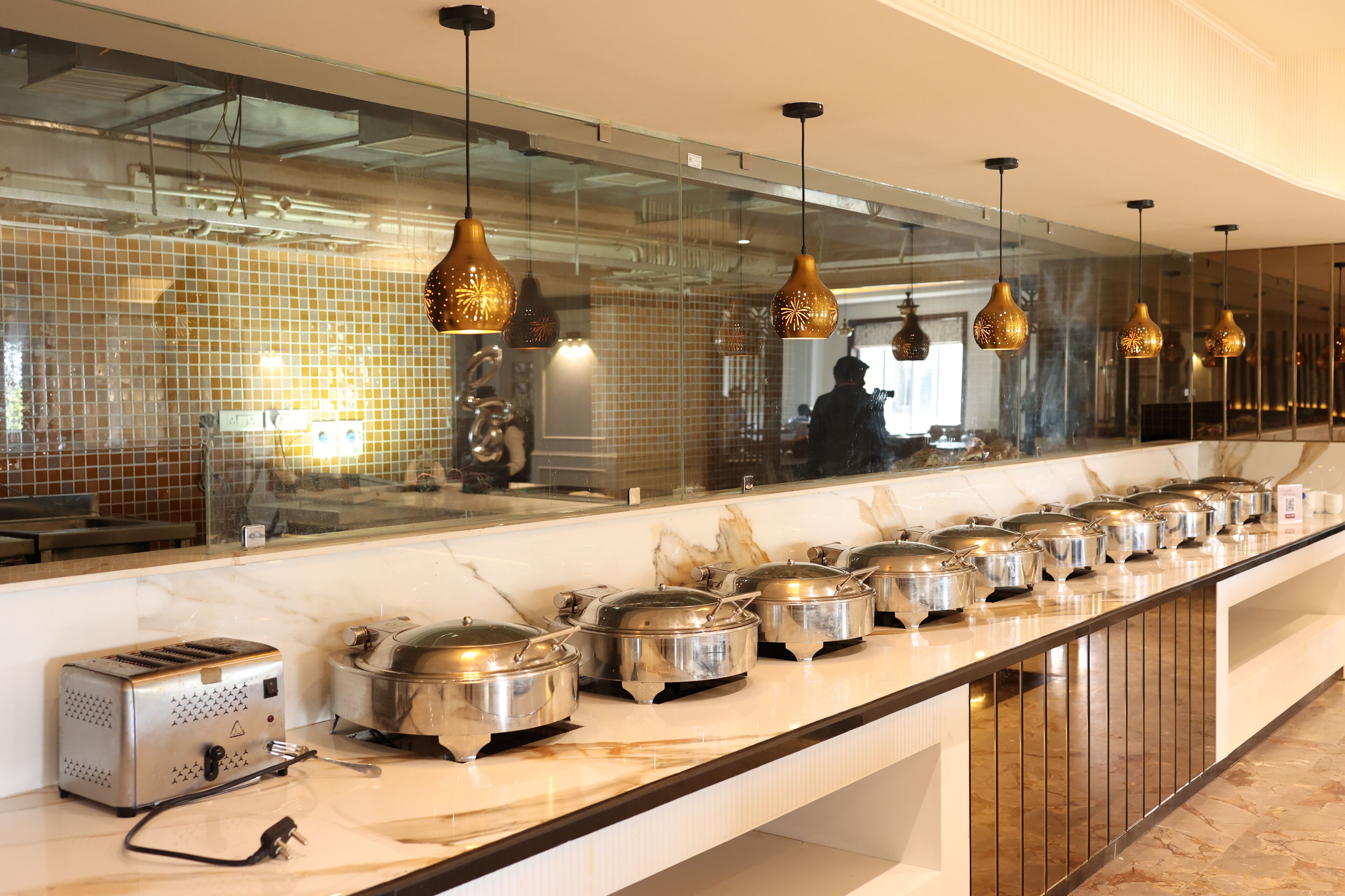 A buffet setup with multiple food containers and a toaster on a marble countertop.