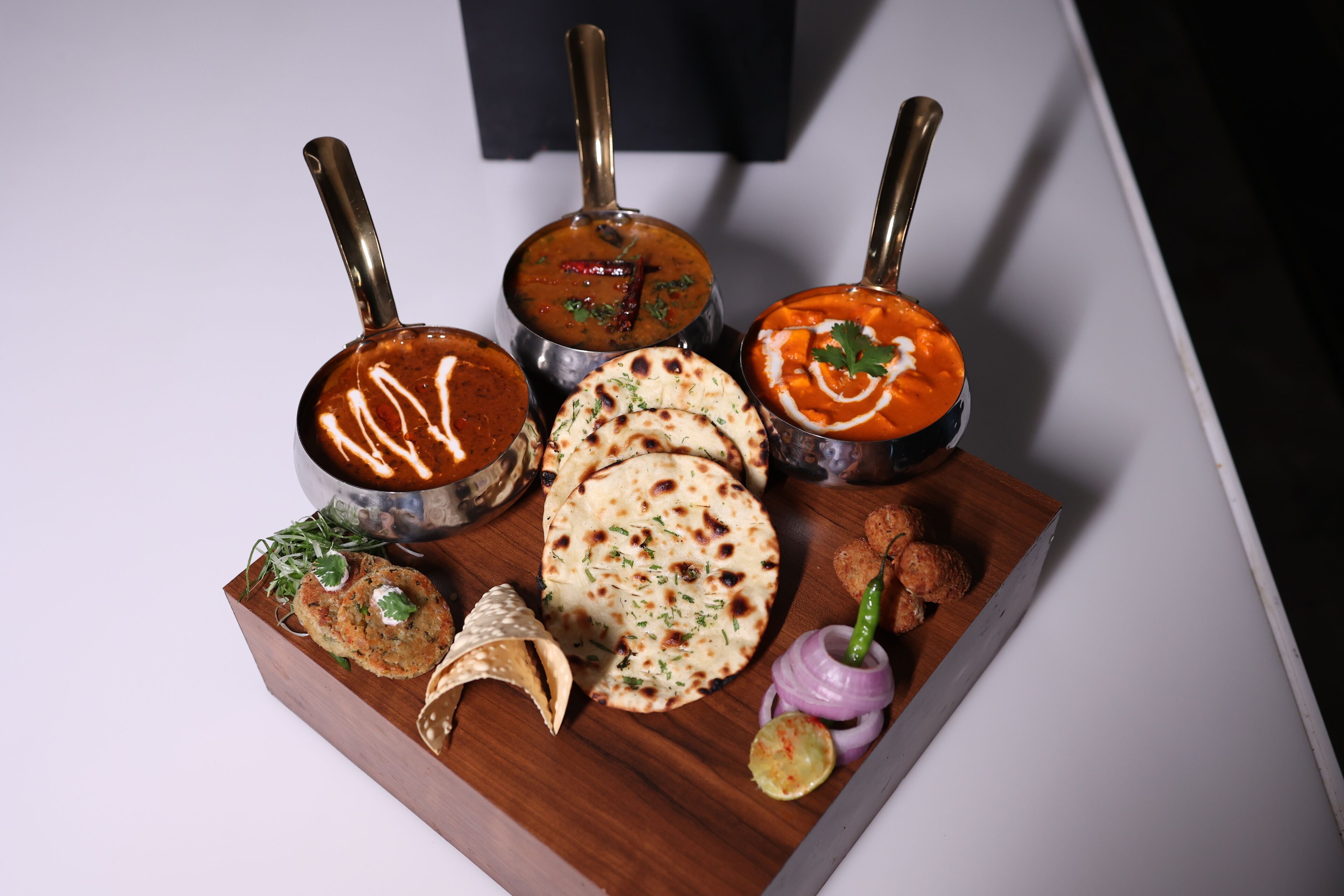 Une planche en bois sur laquelle sont disposés divers plats indiens, notamment des currys et des pains plats, ainsi qu'un petit bol de sucreries.