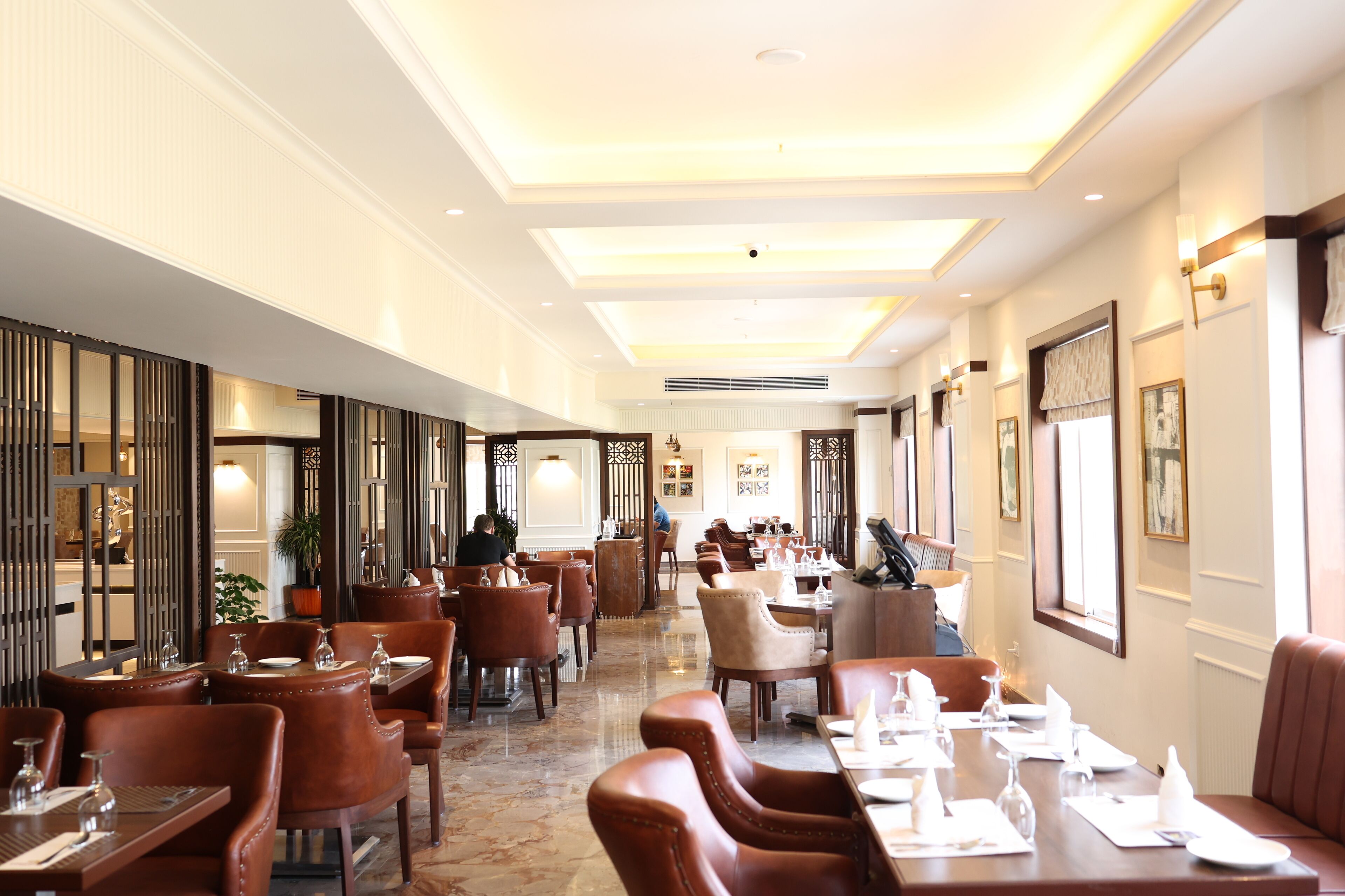 A spacious hotel dining area with multiple tables and chairs, a polished floor, and a high ceiling with recessed lighting.