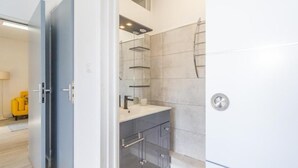 Ein modernes Badezimmer mit grauem Waschtisch, einer Dusche mit Glastür und einem weißen Waschbecken.