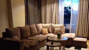 A modern living room with a brown sectional sofa, a small round table, and a patterned rug. - Stay.Plus Nova Apartment Westlands (Nairobi)