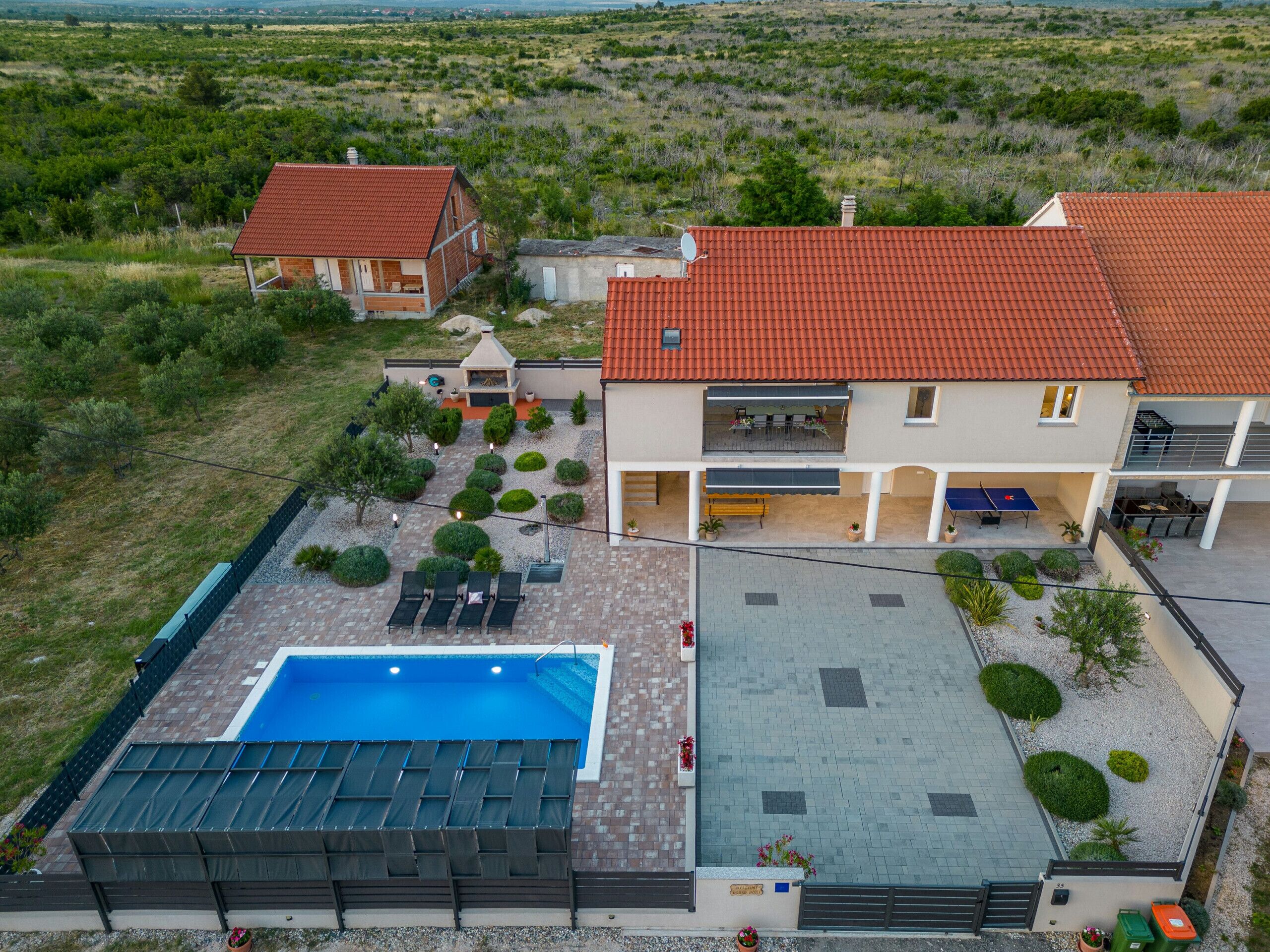 A two-story house with a red-tiled roof, a swimming pool, and a patio area with outdoor furniture.