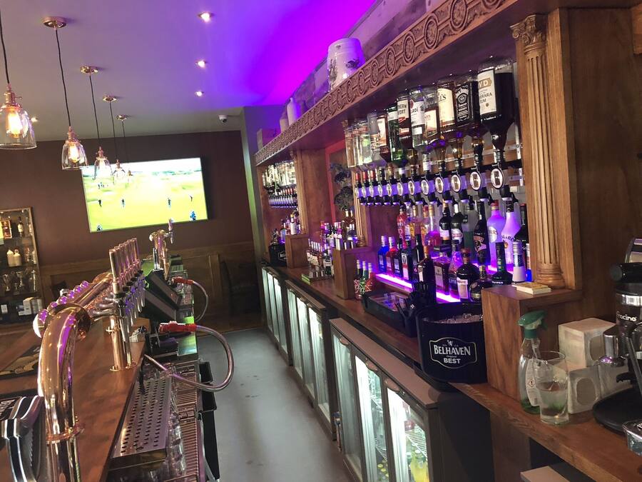 A bar area with a long counter, multiple taps, and a variety of liquor bottles.
