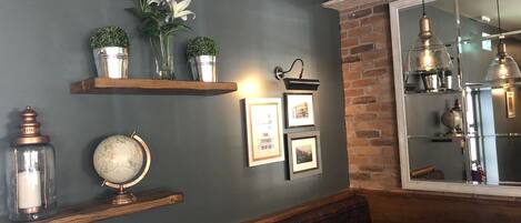 A cozy room with a dark gray wall, wooden shelves with plants, a globe, framed pictures, and a plaid bench.