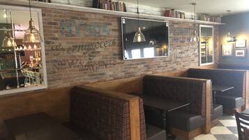 A cozy restaurant with brick walls, wooden benches, and a TV mounted on the wall.