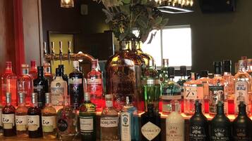 Un bar con diversas botellas de licores, incluyendo ginebra y whisky, y una lámpara colgante.