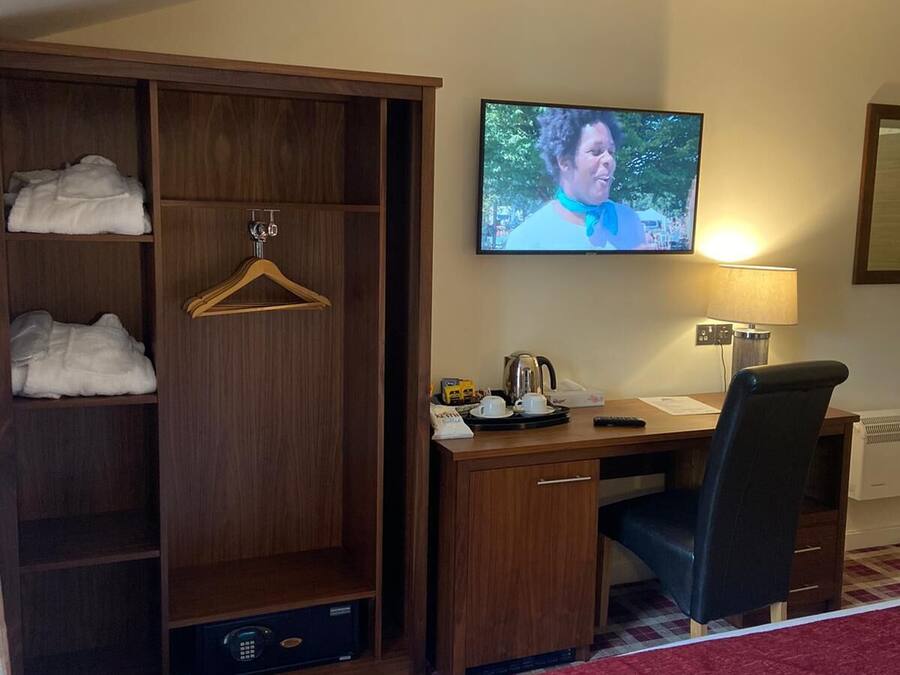 Ein Hotelzimmer mit einem Bett, einem Schreibtisch mit Stuhl, einem Fernseher, einem Kleiderschrank und einem roten Teppich.