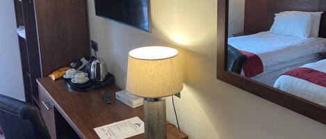 Habitación de hotel con escritorio, lámpara, televisor, cama y espejo que refleja la habitación.