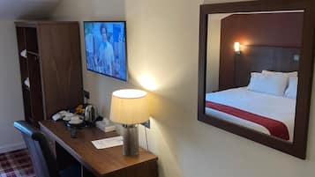 A hotel room with a desk, chair, television, bed, and a radiator.