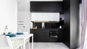 A modern kitchen with black cabinets, a white dining table, and a striped curtain. - Spacious Apartment with Parking | 3 Bedrooms (Gdansk)