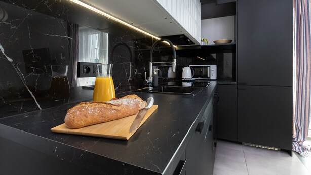 A modern kitchen with a marble countertop, a loaf of bread, a cutting board, and a glass of orange juice. - Spacious Apartment with Parking | 3 Bedrooms (Gdansk)