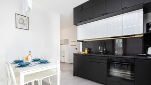 A modern kitchen with black cabinets, a built-in oven, and a dining area with a white table and blue plates. - Spacious Apartment with Parking | 3 Bedrooms (Gdansk)
