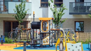A playground with various play structures, surrounded by a building with large windows and a balcony. - Spacious Apartment with Parking | 3 Bedrooms (Gdansk)