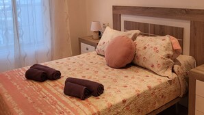 Ein Schlafzimmer mit einem Bett, Kissen, einem Nachttisch, einer Lampe und zwei floralen Bildern an der Wand.