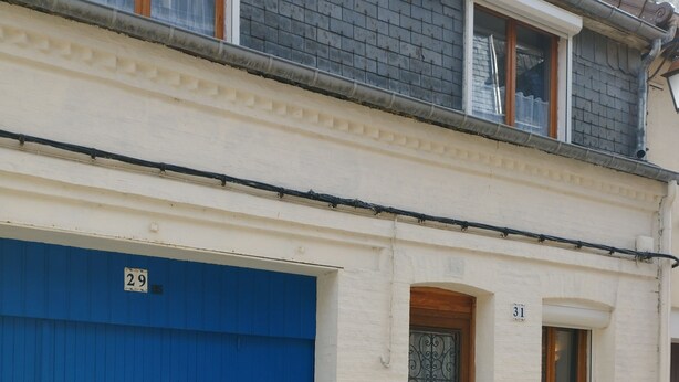 Un edificio con puerta de garaje azul numerada 29, una puerta de madera con ventana y una ventana pequeña con cortina.