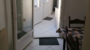 Un pasillo estrecho con suelo de baldosas, una puerta que da a una habitación y una pequeña mesa con mantel estampado.