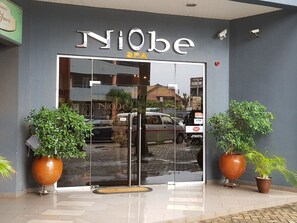 The entrance to Niobe Spa with a glass door, two large potted plants, and a security camera on the wall.