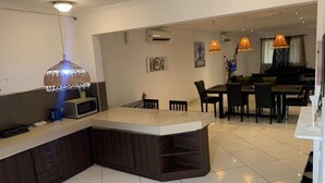 Una cocina moderna con una isla central, armarios de madera oscura y un microondas. Hay una zona de comedor con una mesa y sillas, además de lámparas colgantes.