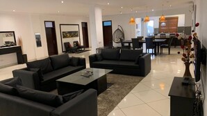 Una sala moderna con sofás negros, una mesa de centro y un comedor con una araña.