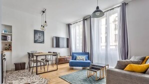 A modern living room with a dining area, a blue armchair, a grey sofa, and a flat-screen TV.