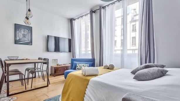 A hotel room with a bed, a desk, a chair, a TV, and a window with curtains.
