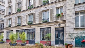 A building with multiple windows, some with shutters, and a cobblestone courtyard with potted plants. - NEW Design Flat in the Heart of Paris-An Ecoloflat (Paris)