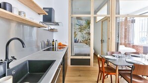A modern kitchen with a black sink, wooden shelves, and a dining area with a table set for four. - NEW Design Flat in the Heart of Paris-An Ecoloflat (Paris)