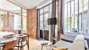 A modern living room with a brick wall, a sofa, a dining table set, and a TV. - NEW Design Flat in the Heart of Paris-An Ecoloflat (Paris)