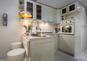 A modern kitchen with white cabinets, a built-in oven, a sink, and a small island with stools.