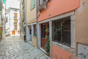 A narrow cobblestone street flanked by buildings with balconies and wooden shutters.