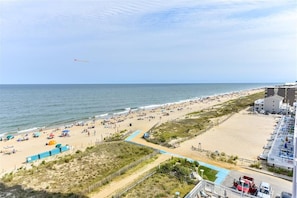Una playa con una larga extensión de arena, algunos sombrillas y unas pocas personas. Se observa un edificio de varios pisos al lado derecho.