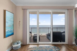 Una habitación con un amplio ventanal corredera que da a un balcón con mobiliario exterior y vistas al océano.