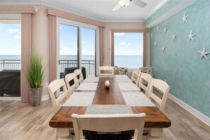 Un comedor con una mesa y sillas de madera, ventanas amplias con vista al océano y un ventilador de techo.