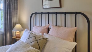 A neatly made bed with a headboard, a bedside lamp, and a framed picture on the wall. - gold miners cottage (Lancefield)