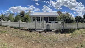 A white house with a picket fence, surrounded by trees and a clear sky. - gold miners cottage (Lancefield)