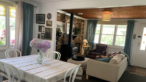 A cozy living room with a dining table, chairs, a sofa, a fireplace, and a view of greenery outside. - gold miners cottage (Lancefield)