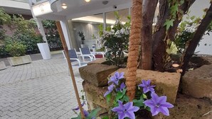 A sign for 'ROYAL PLAZA' with a planter of purple flowers and a tree. - Hotel Royal Plaza (Rimini)