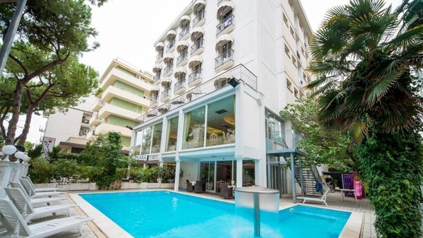 A swimming pool with lounge chairs, a covered area with tables, and a building with balconies in the background. - Hotel Royal Plaza (Rimini)