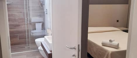 Een moderne hotelkamer met houten vloer, een bed met witte dekbedovertrek, een badkamer met douchecabine van glas en uitzicht op het omliggende landschap.