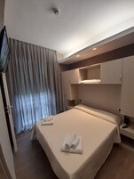 Quarto de hotel com uma cama, televisão e janela com cortinas.