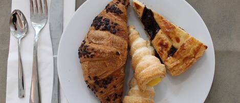 A plate with a croissant and a piece of pie on a white plate.