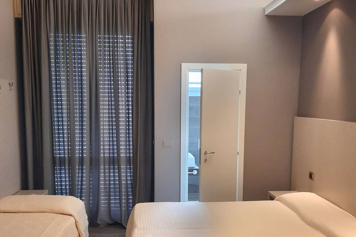 Ett hotellrum med två sängar, ett fönster med gardiner, en dörr och utsikt över omgivningarna.