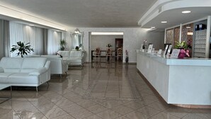 A modern hotel lobby with a reception desk, seating area, and a dining space. - Hotel Royal Plaza (Rimini)