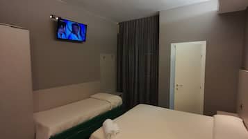 Una habitación de hotel con dos camas individuales, un televisor en la pared, una puerta y una cortina.