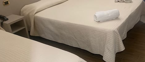Una habitación de hotel con dos camas, una mesita de noche con teléfono, y una puerta que da a otra estancia.