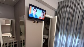 A hotel room with a bed, a TV mounted on the wall, a desk with a chair, and a bathroom visible through an open door. - Hotel Royal Plaza (Rimini)