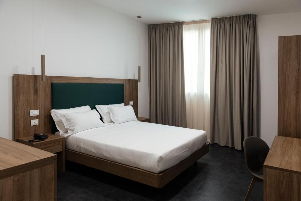 Ein Hotelzimmer mit hölzernem Bettgestell, weißer Bettwäsche, einem Schreibtisch und einem Stuhl.