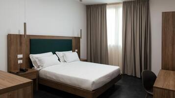 Ein Hotelzimmer mit hölzernem Bettgestell, weißer Bettwäsche, einem Schreibtisch und einem Stuhl.